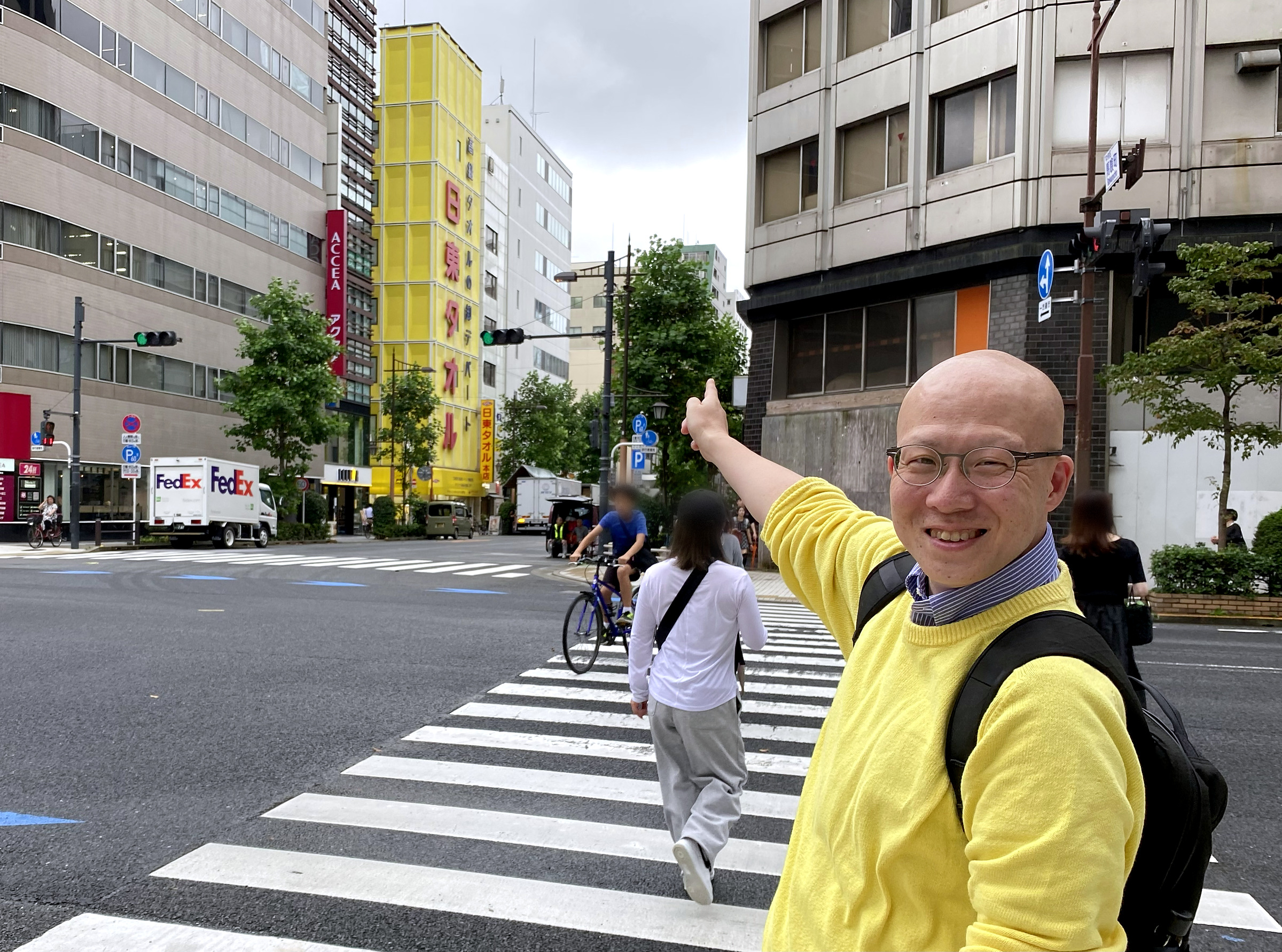 横山町の交差点から黄色いビルを指さす鳥山さん